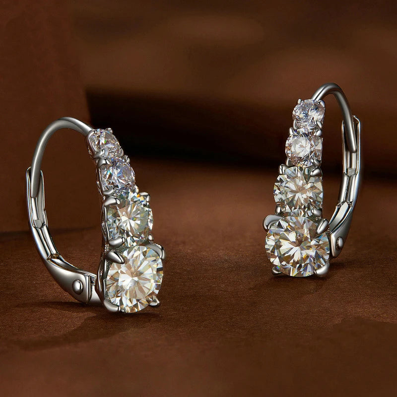 Une paire de boucles d'oreilles à clous en argent sterling 925 et moissanite, présentées sur une surface marron.
