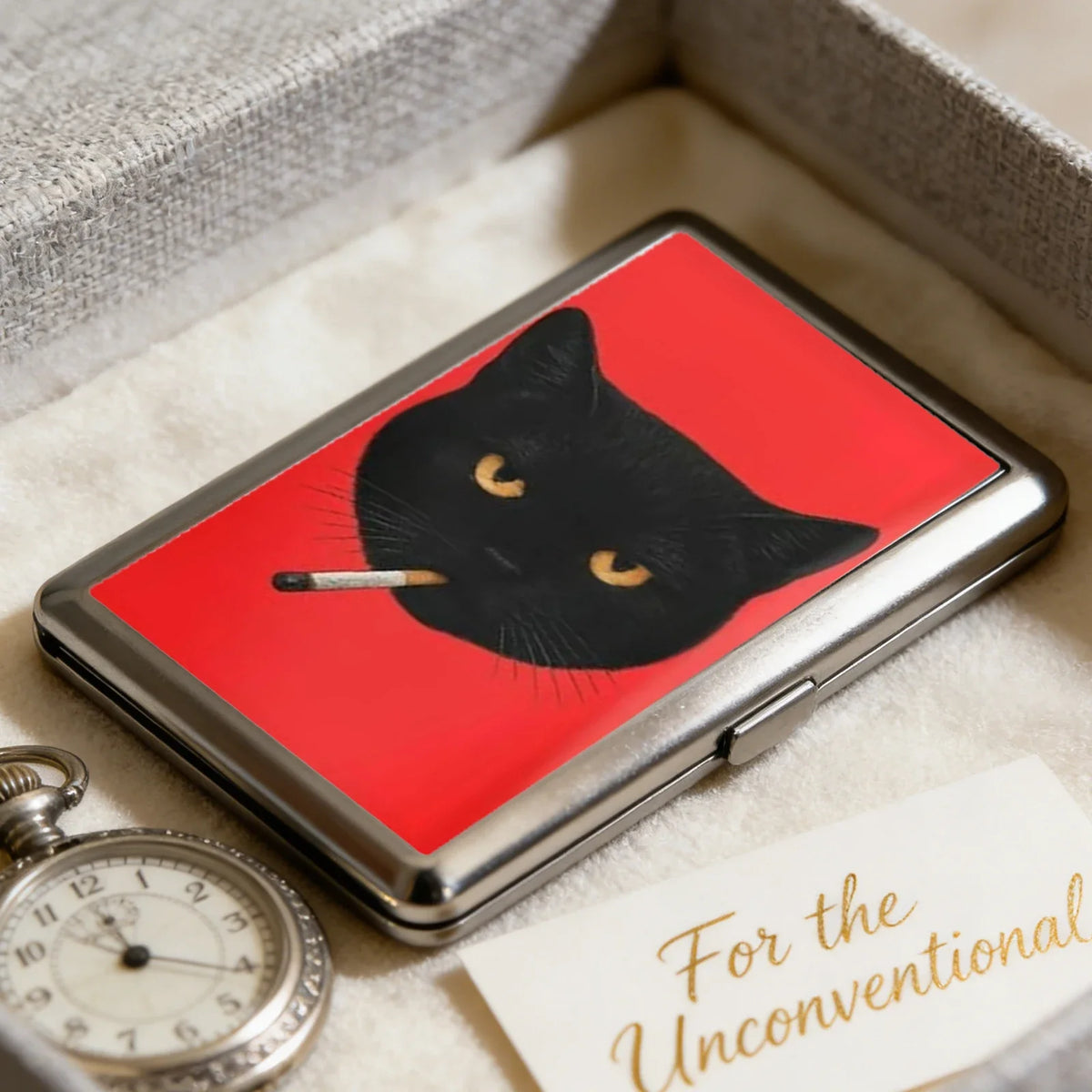 A vintage metal card and cash case featuring a black cat silhouette on a red background resting on a light fabric.