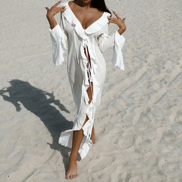 A woman wearing a white chiffon beach cover-up tunic with ruffled sleeves walking on the sand.