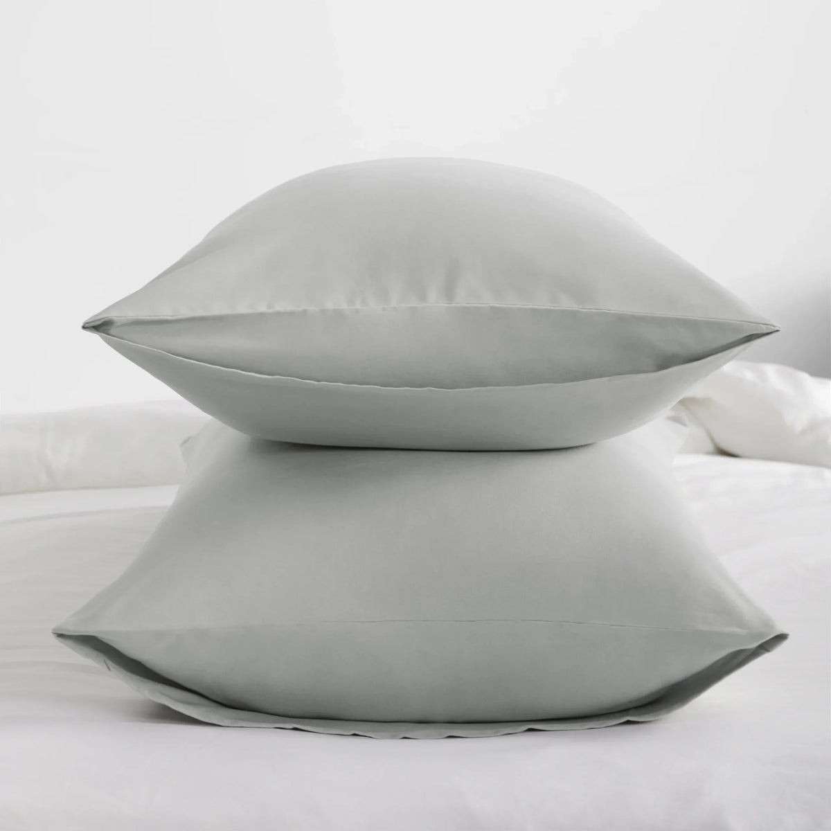 A set of four solid gray microfiber pillowcases with envelope closure resting on a white bed.