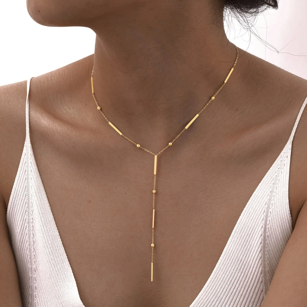 Primer plano de un collar de lariat dorado superpuesto, usado alrededor del cuello sobre un tono de piel neutro.