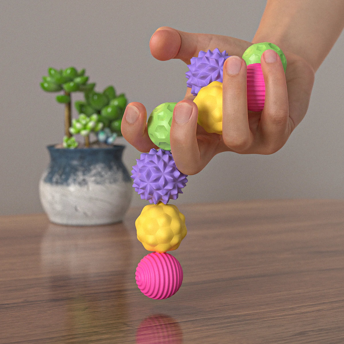 A hand holds a string of colorful magnetic silicone fidget balls, including purple, yellow, and pink.