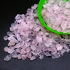 A pile of pink and clear tumbled crystal stone chips in a green bowl.