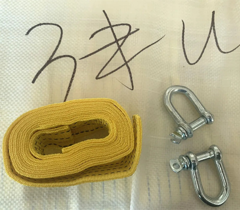 A yellow heavy-duty vehicle recovery towing strap coiled on a light surface next to metal tow shackles.