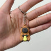 A small keychain charm of a brown capybara bear with yellow accents, held in a person's hand.