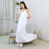 A woman wearing a white maxi dress is sitting on a chair indoors.