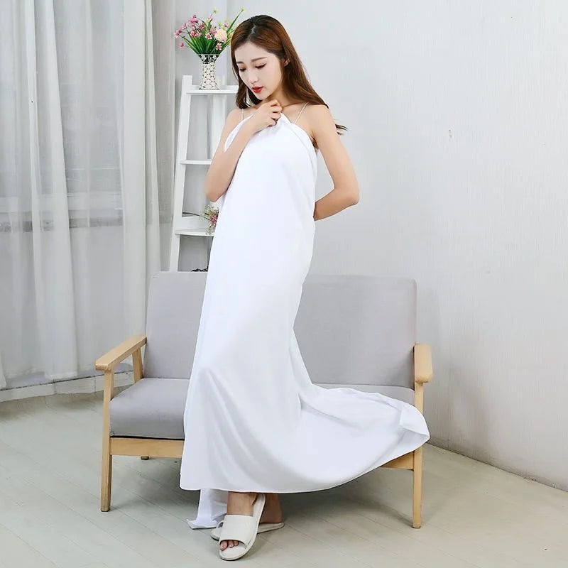 A woman wearing a white maxi dress is sitting on a chair indoors.