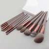 A set of thirteen makeup brushes in various shades of brown and rose are displayed next to a white travel bag.