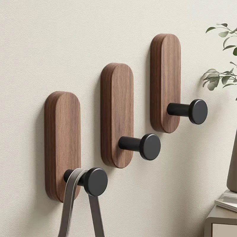 A set of self-adhesive walnut wood hooks mounted on a wall for entryway or bathroom organization.