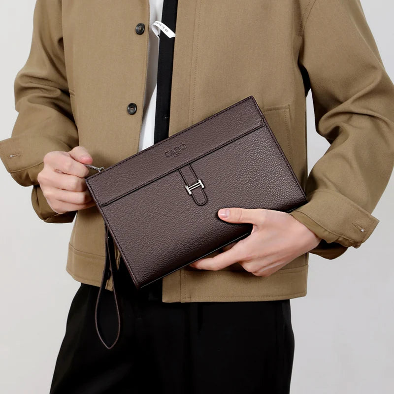 Eine Frau hält eine dunkelbraune Kunstleder-Clutch vor einer beige Jacke.