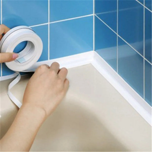 Une main applique une bande de scellement en silicone blanc sur le coin d'une baignoire ou d'un lavabo carrelé de bleu.