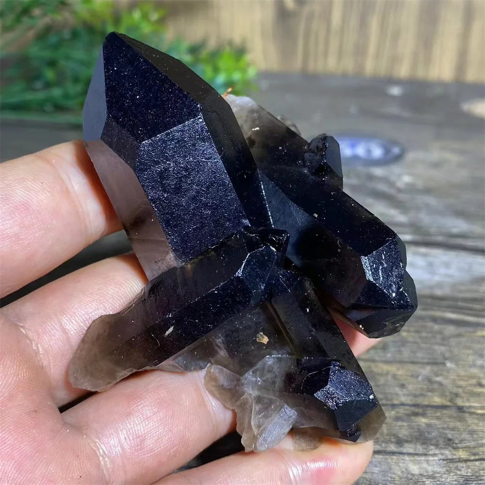 A cluster of dark purple and smoky quartz crystals held in a hand.