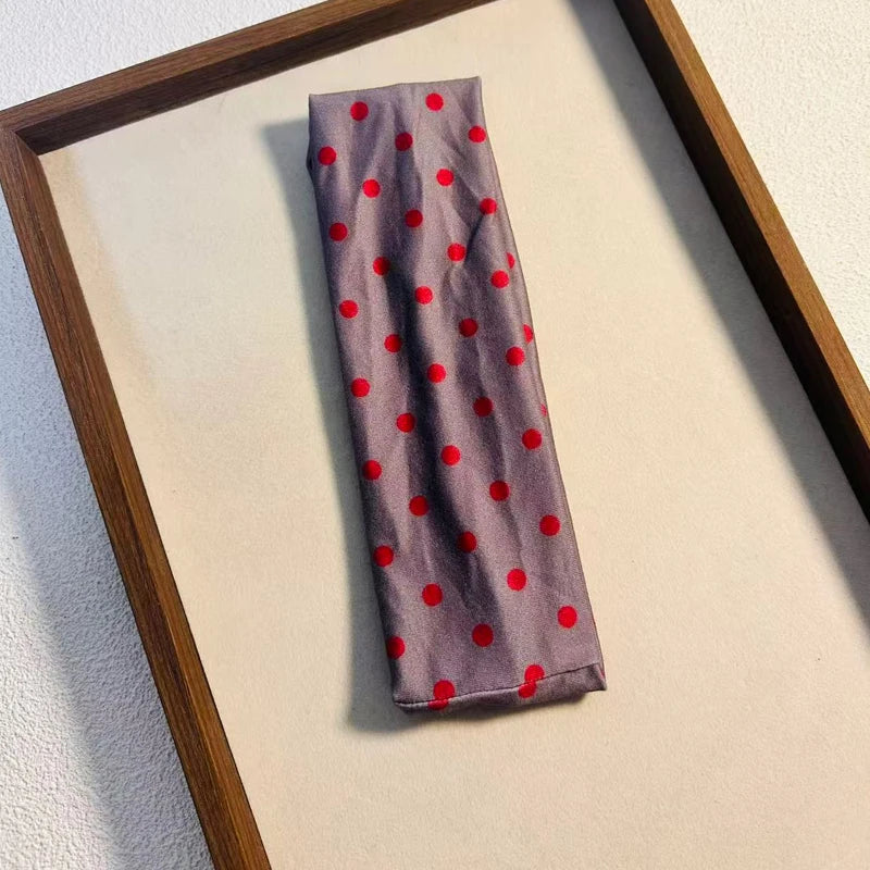 Bandeau en tissu violet avec petits pois rouges, exposé dans un cadre en bois.