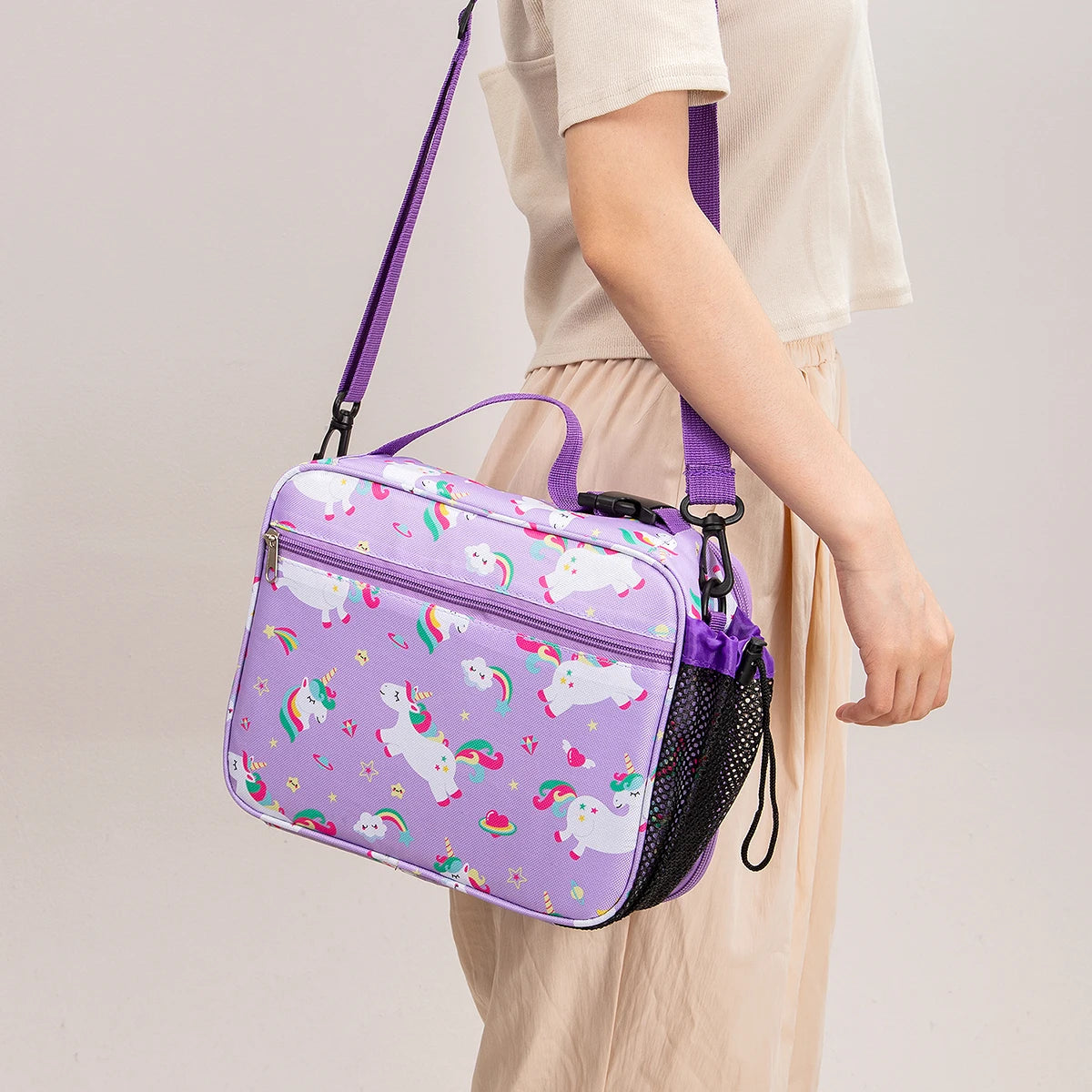 A purple and white unicorn patterned insulated lunch bag with a purple strap is being held by a person.