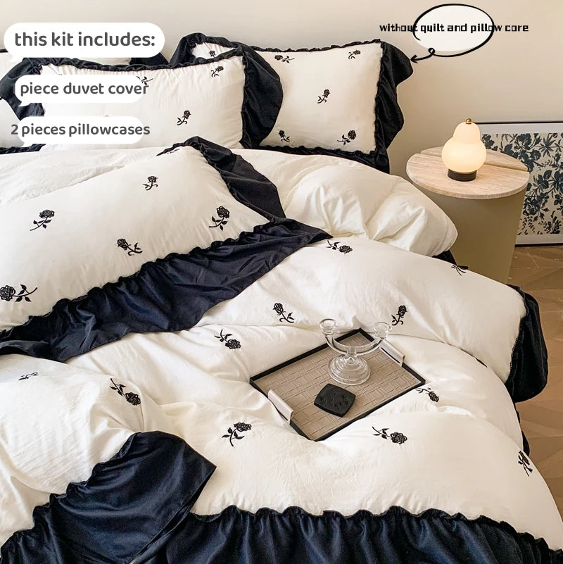 A set of black and white rose embroidered duvet covers, pillowcases, and a matching bed skirt.