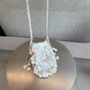 A white sequin accent chain shoulder bag with a woven strap displayed on a round pedestal.