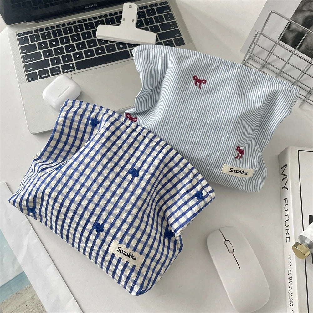 A blue plaid makeup bag with floral embroidery is shown next to a laptop and a white wireless mouse.