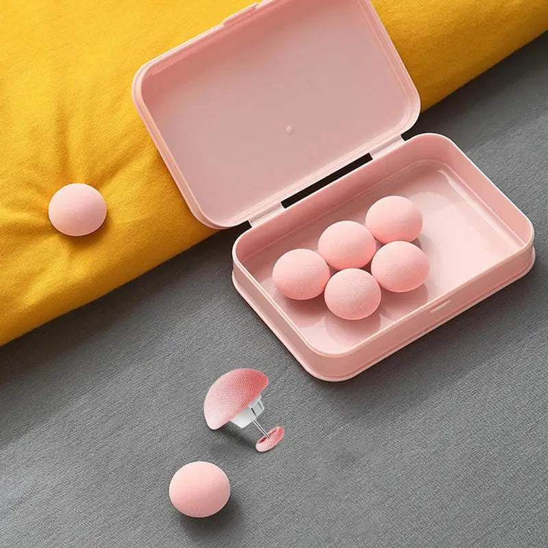 A pink storage box with six pink round clips rests on a yellow fabric surface.