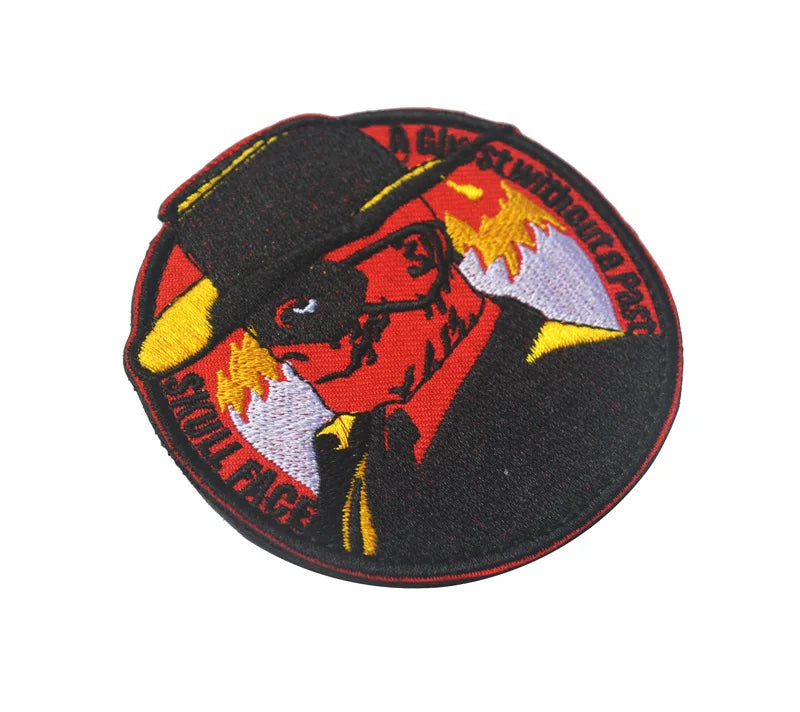 An embroidered patch featuring a stylized foxhound face wearing a hat and surrounded by flames on a black background.