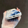 A hand holds a white phone case featuring blue floral designs against a dark background.