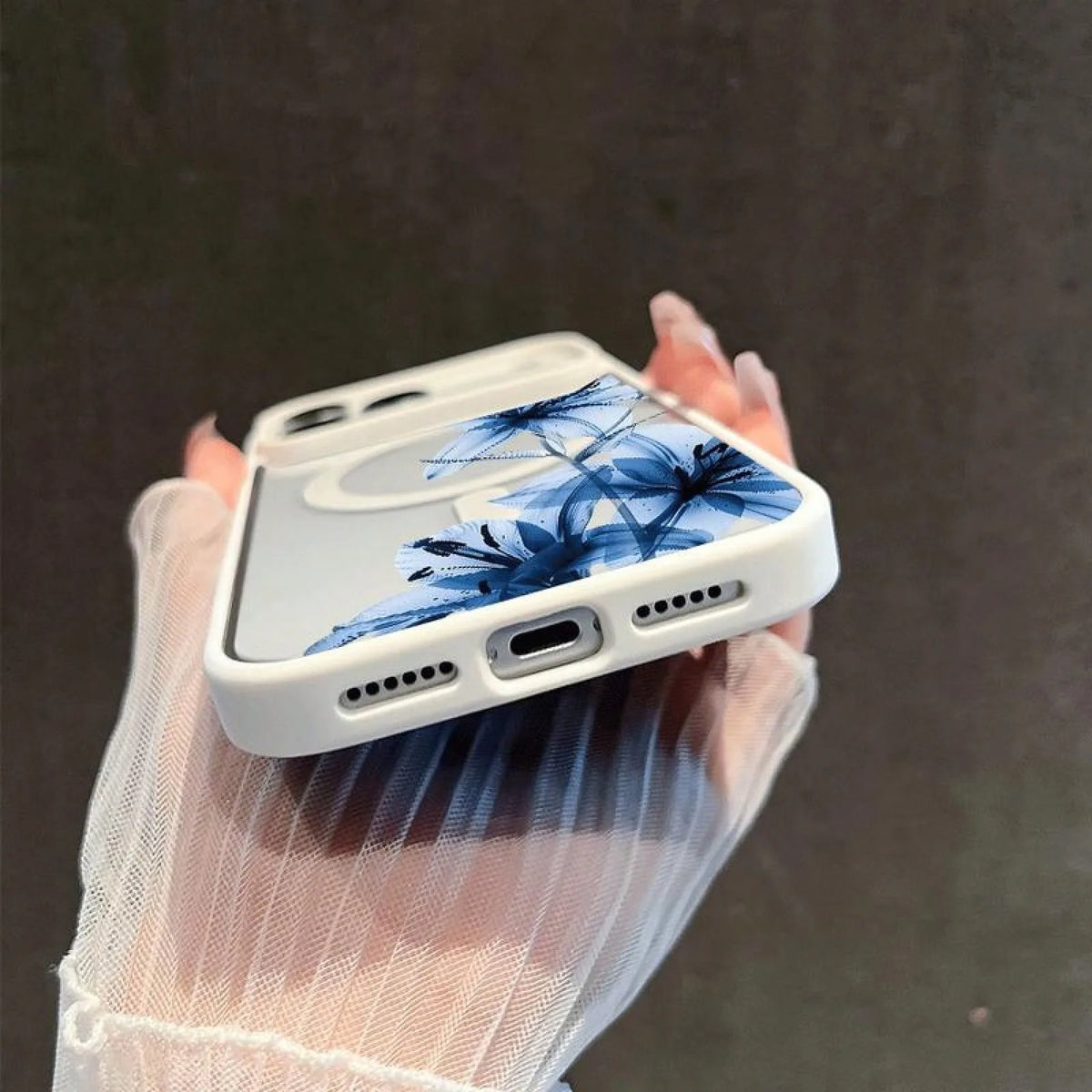 A hand holds a white phone case featuring blue floral designs against a dark background.