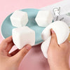 A hand holds a white squishy milk tofu fidget toy against a light blue plate.