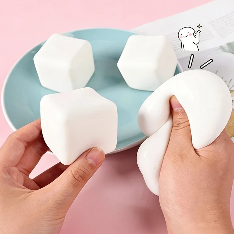 A hand holds a white squishy milk tofu fidget toy against a light blue plate.