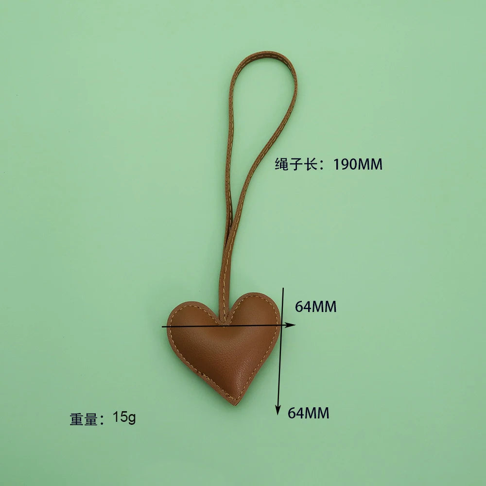 A brown heart-shaped PU leather keychain with a cotton peach charm, shown against a light green background.