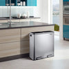 A stainless steel dual compartment recycling trash can with a soft-close lid sitting on a kitchen counter.