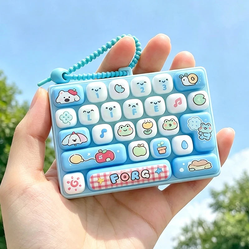 A hand holds a light blue cartoon keycap fidget keychain with various colorful icons and a blue beaded chain.