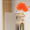 An extendable microfiber duster with an orange fluff head is shown removing dust from the top of a cabinet shelf.