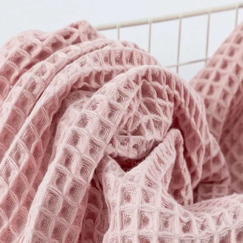 A close-up of a pink waffle weave bath towel draped and folded on a hanger.