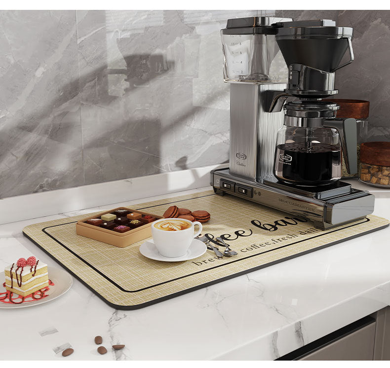 A silver coffee grinder and a natural fiber coffee mat are displayed on a white countertop.