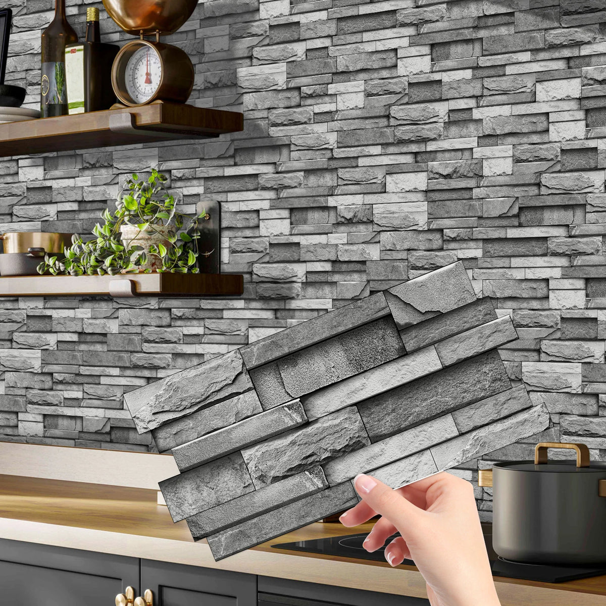 A hand holds a stack of gray stone tile stickers against a gray stacked stone wall background.
