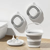 A white foldable portable wash basin with a handle is displayed on a wooden surface next to stacked gray basins.