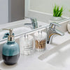 A set of clear storage jars with lids containing cotton swabs and other beauty tools on a white bathroom sink.