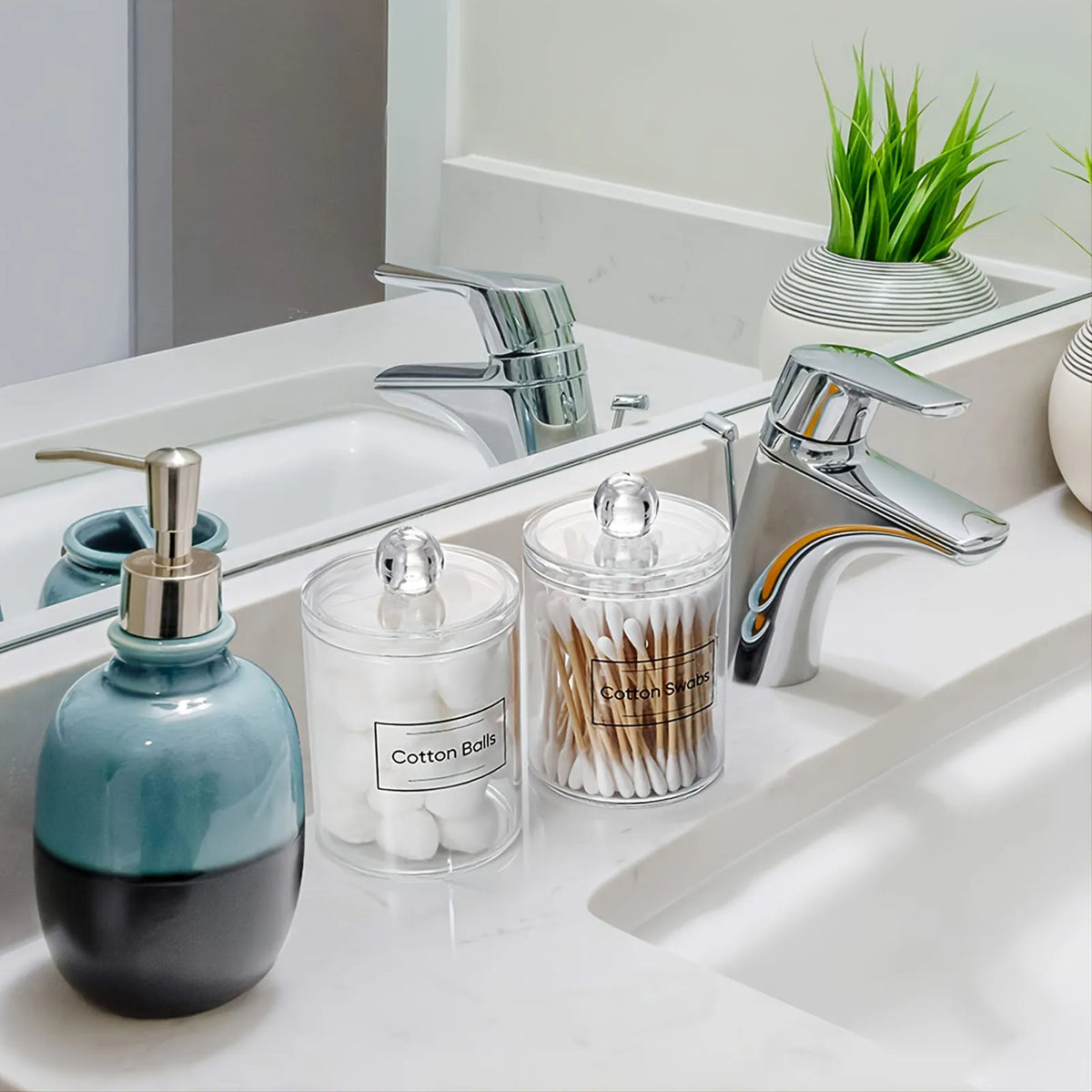 A set of clear storage jars with lids containing cotton swabs and other beauty tools on a white bathroom sink.