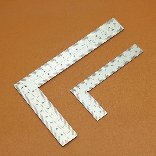A stainless steel framing square with dual scales laid diagonally on a brown surface.