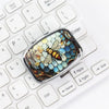 A portable metal pill organizer and jewelry case with a hexagonal, iridescent design resting on a white keyboard.