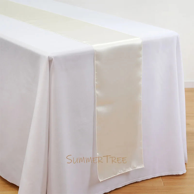 Elegant satin table runner in cream color draped across a white tablecloth.