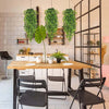 A dining table set with black chairs and artificial green hanging vines decorating a white brick wall.