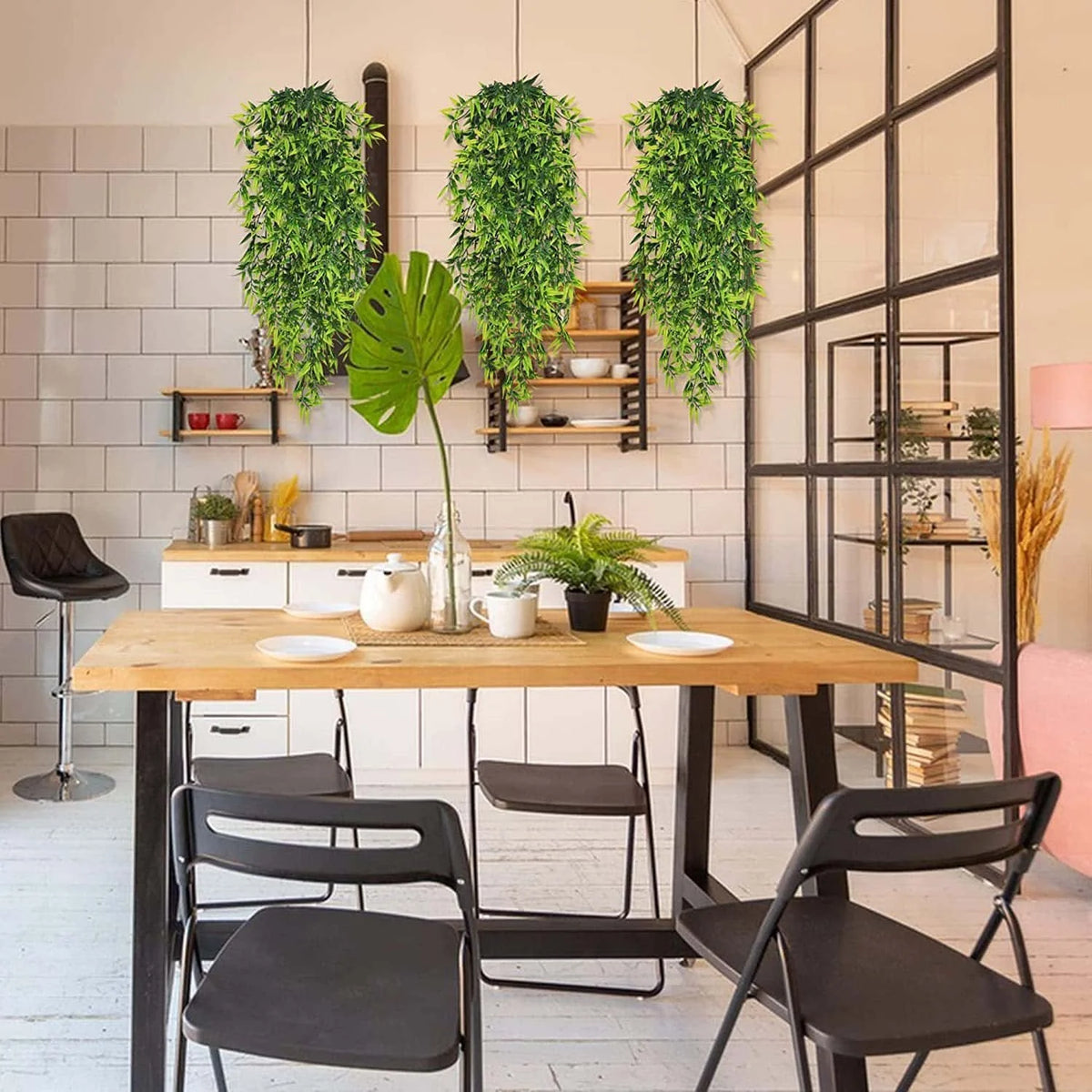A dining table set with black chairs and artificial green hanging vines decorating a white brick wall.