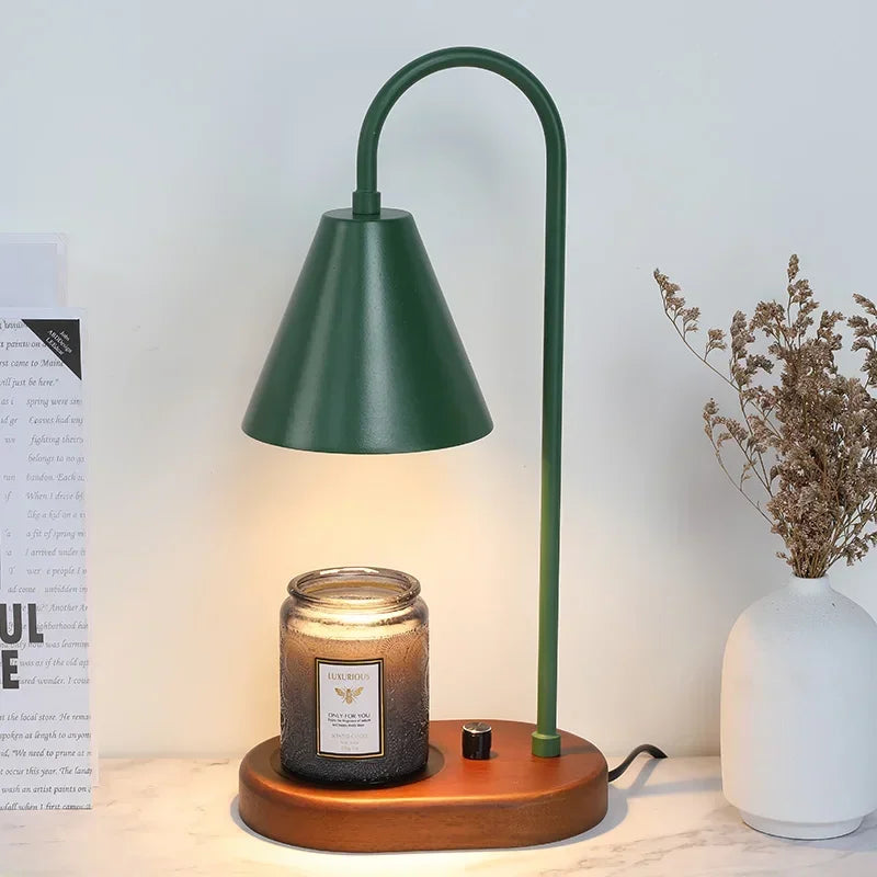 A tall, dark green electric candle warmer lamp with a conical shade and wooden base sits on a white surface.