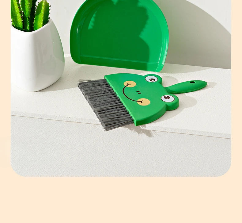 A set of green cartoon-themed cleaning tools including a broom and a dustpan resting on a white surface.