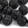A close-up view of small, round black crystal clay beads scattered on a white surface.