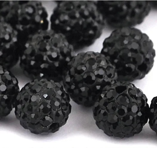 A close-up view of small, round black crystal clay beads scattered on a white surface.