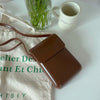 A brown vintage PU leather crossbody shoulder bag resting on a white surface next to a glass of green sticks and a ceramic mu