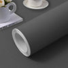 A roll of white self-adhesive peel-and-stick wallpaper lying on a gray surface next to a white mug and a book.
