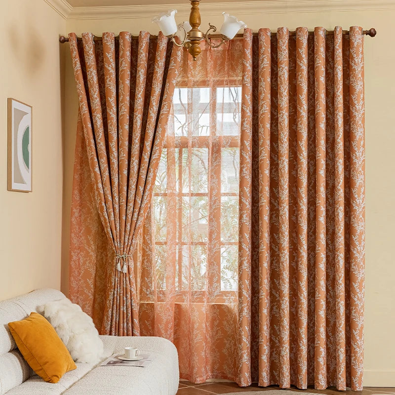 A set of orange patterned blackout curtain panels with grommet tops hanging in a window.
