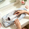 A hand is opening a quilted cotton hair dryer storage bag with a handle, revealing a white hair dryer inside.